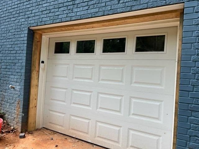 White garage door with windows, framed by wooden trim against a blue brick wall.