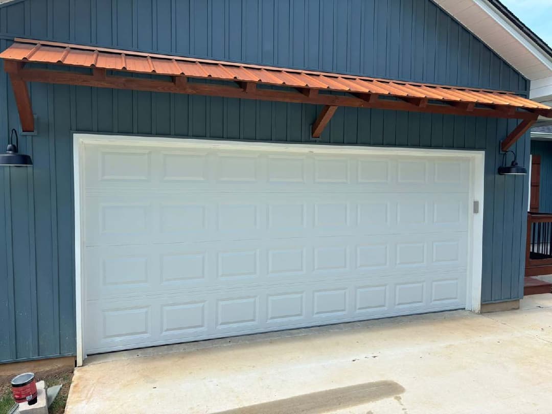 White garage door with wooden overhang on blue house exterior.