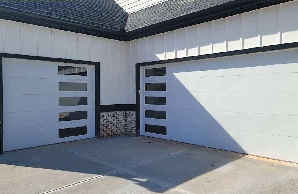 Modern two-car garage with sleek white doors and decorative windows, set against a light exterior.