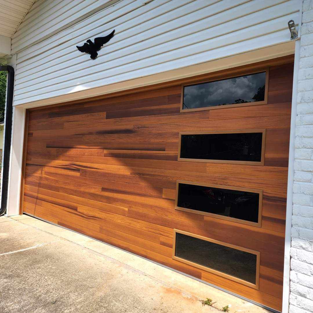 Modern wooden garage door with glass panels and sleek design against white house exterior.
