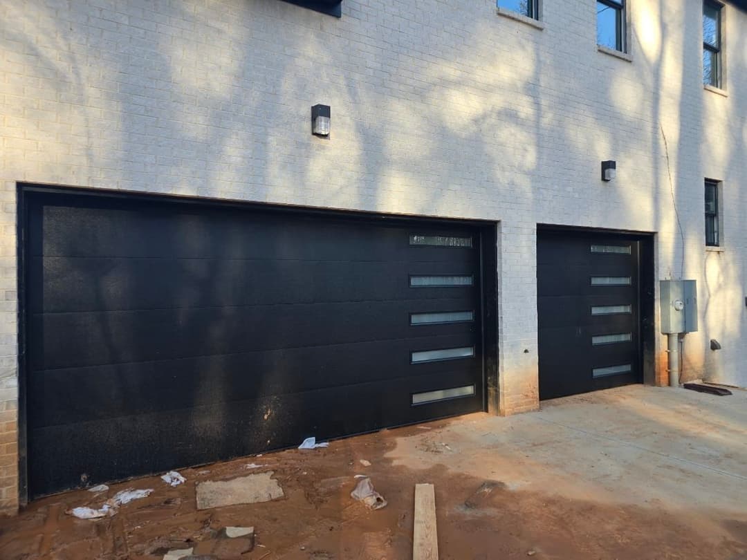 Modern black garage doors with glass panels on a brick home exterior.