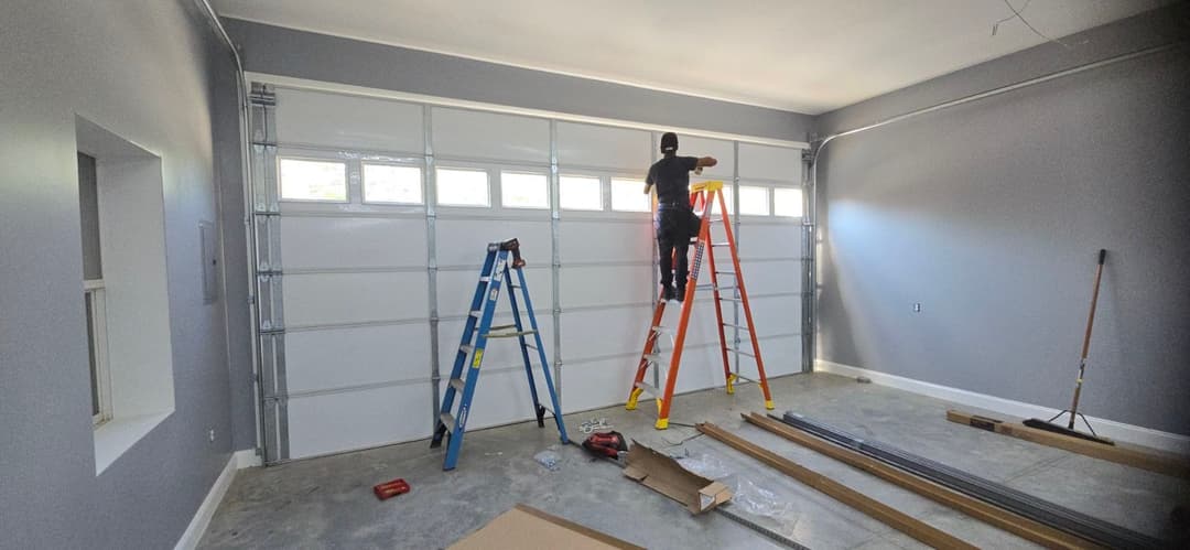 Person installing garage door windows using ladders in a newly painted gray garage.