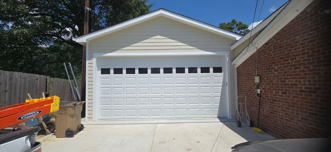 White garage door with windows, modern design, beside brick wall and driveway.