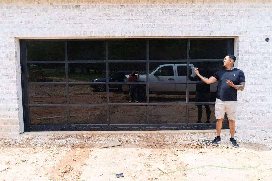 Garage door installation with a man pointing at the modern glass design outside a newly built home.