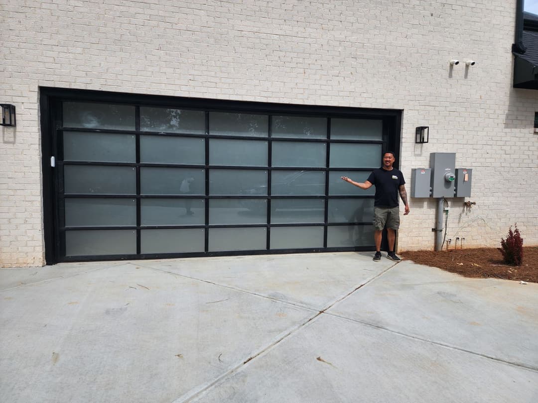 Man standing beside a modern glass garage door on a newly paved driveway.