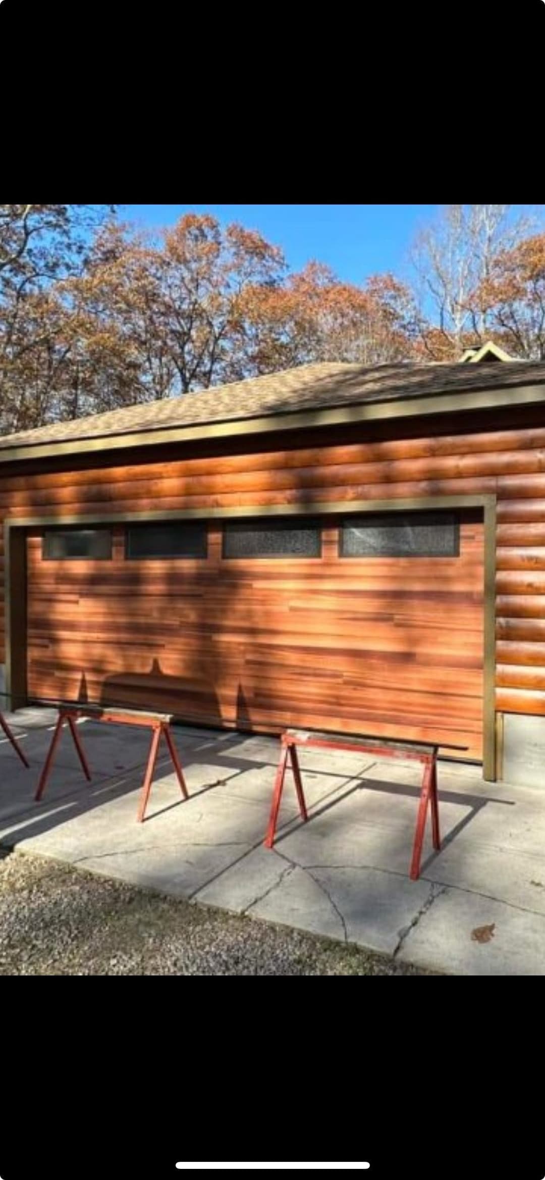 Log cabin garage with wooden siding and large window accents, set in a wooded area.