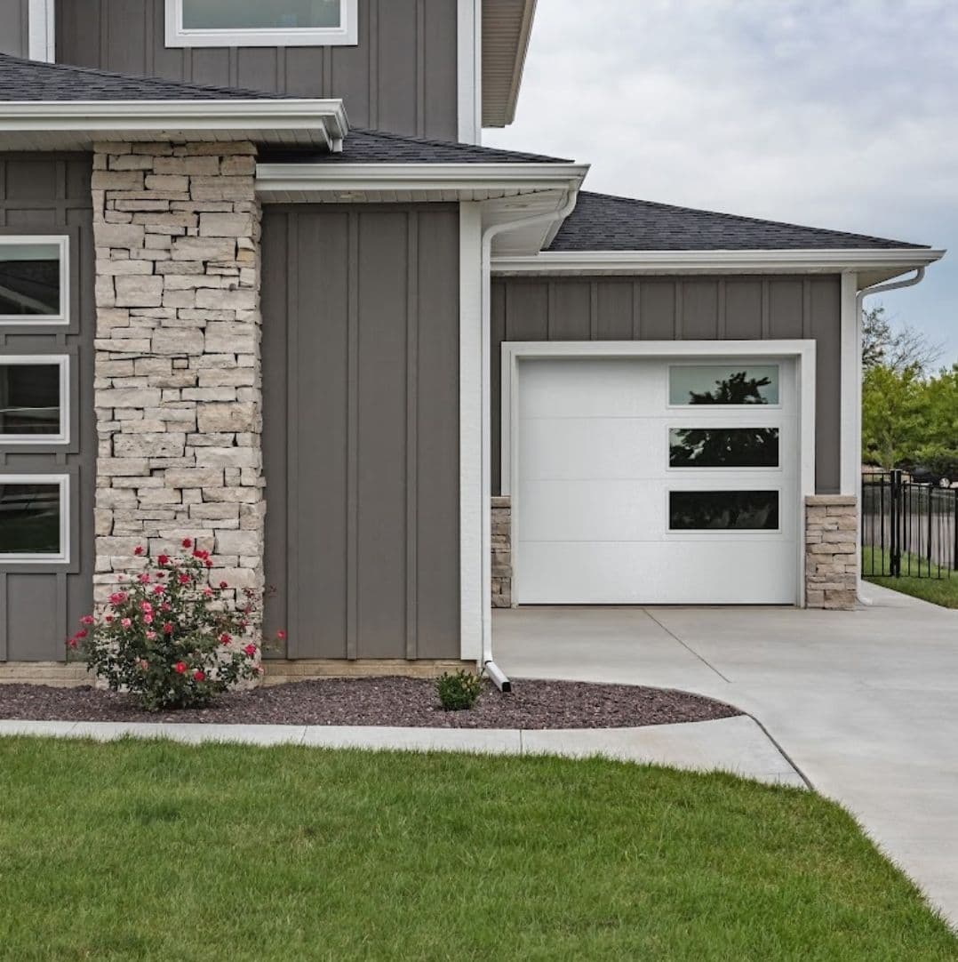 Modern house exterior with stone accents, white garage door, and landscaped yard.