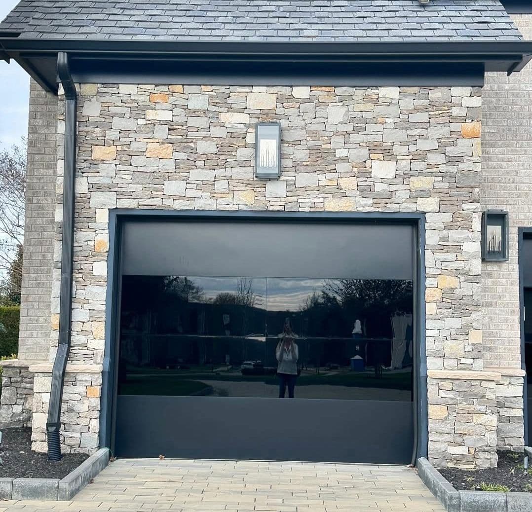 Modern stone garage facade with sleek black garage door and outdoor lighting.