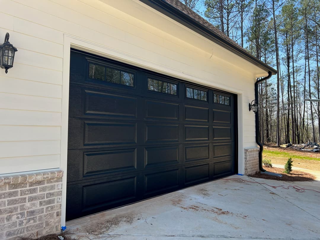 Black garage door with decorative windows, modern home exterior, surrounded by trees.