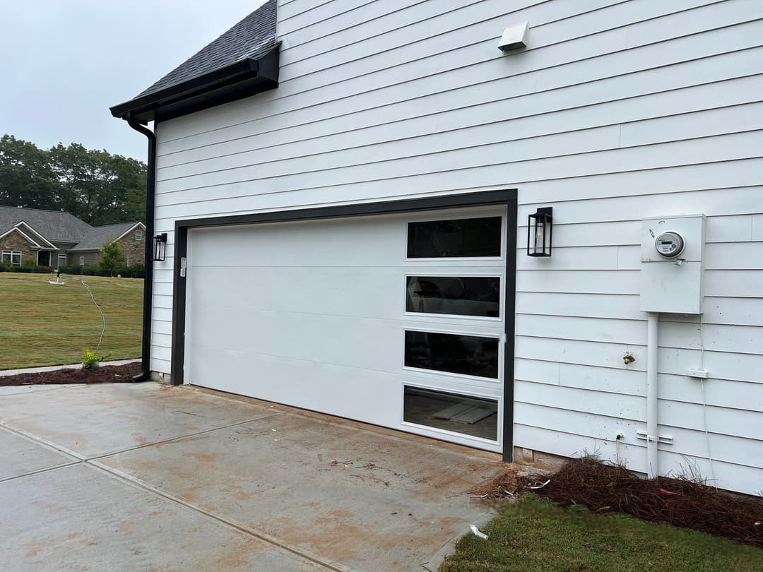 Modern white garage door with glass panels and exterior lighting beside a concrete driveway.