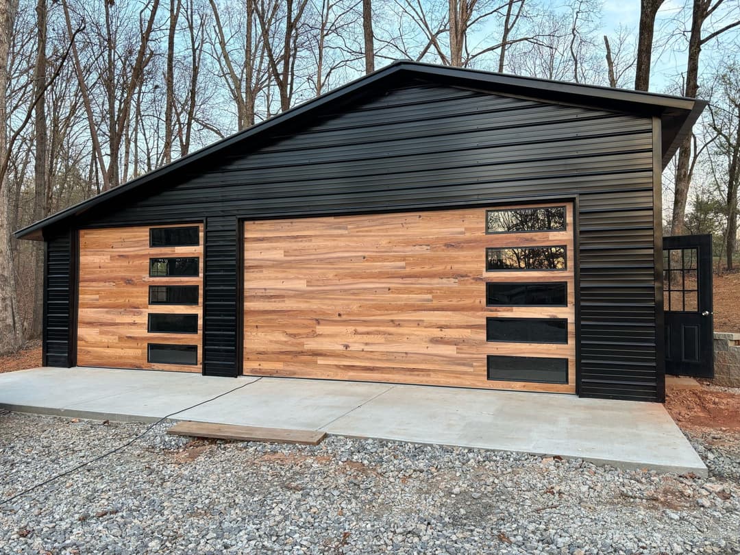 Modern black and wood garage design with large doors, set in a wooded area.