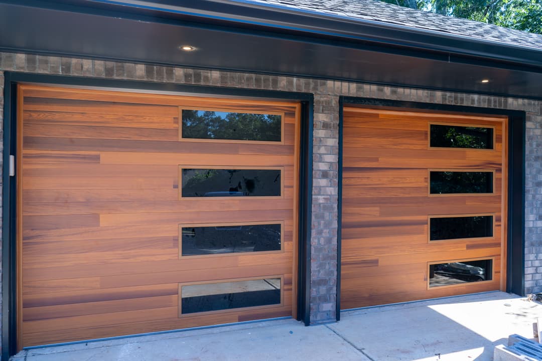 Modern wooden garage doors with horizontal slats and rectangular glass panels.
