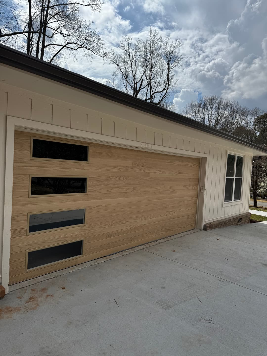 Modern wooden garage door with three glass panels, surrounded by a light-colored home exterior.
