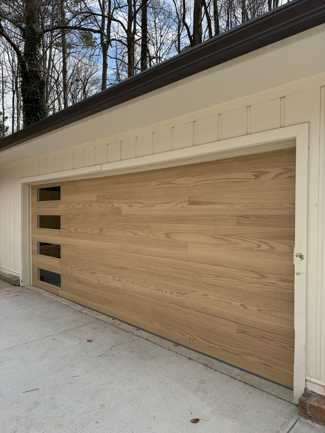 Modern wooden garage door with horizontal panels and glass inserts on a residential home.