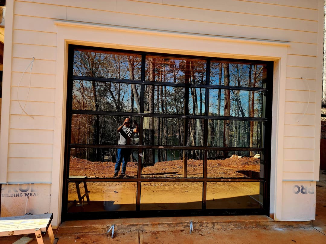 Modern garage door with reflective glass, surrounded by trees and construction site.