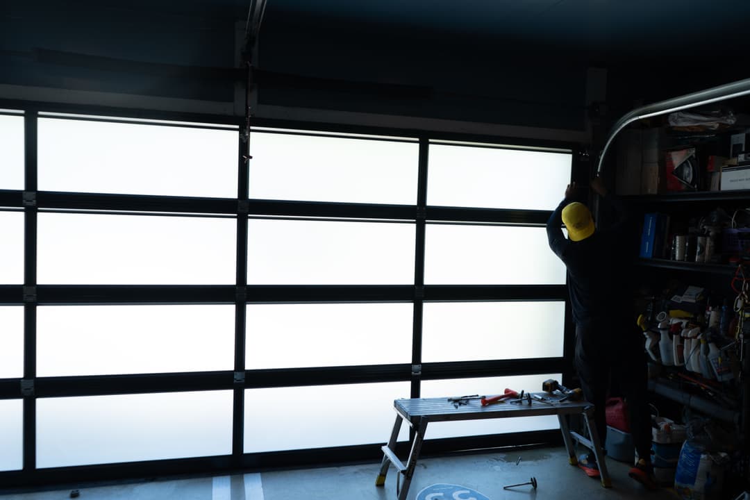 Person installing a garage door in a well-organized garage with tools and supplies.