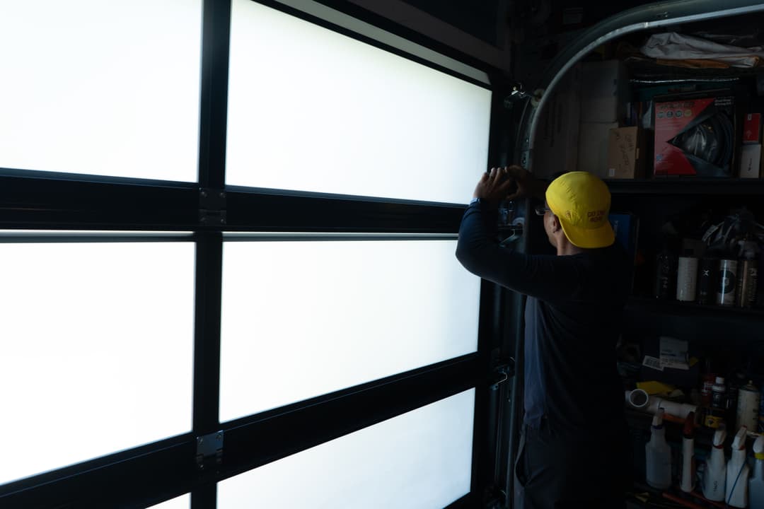Person installing a garage door window while surrounded by tools and supplies.
