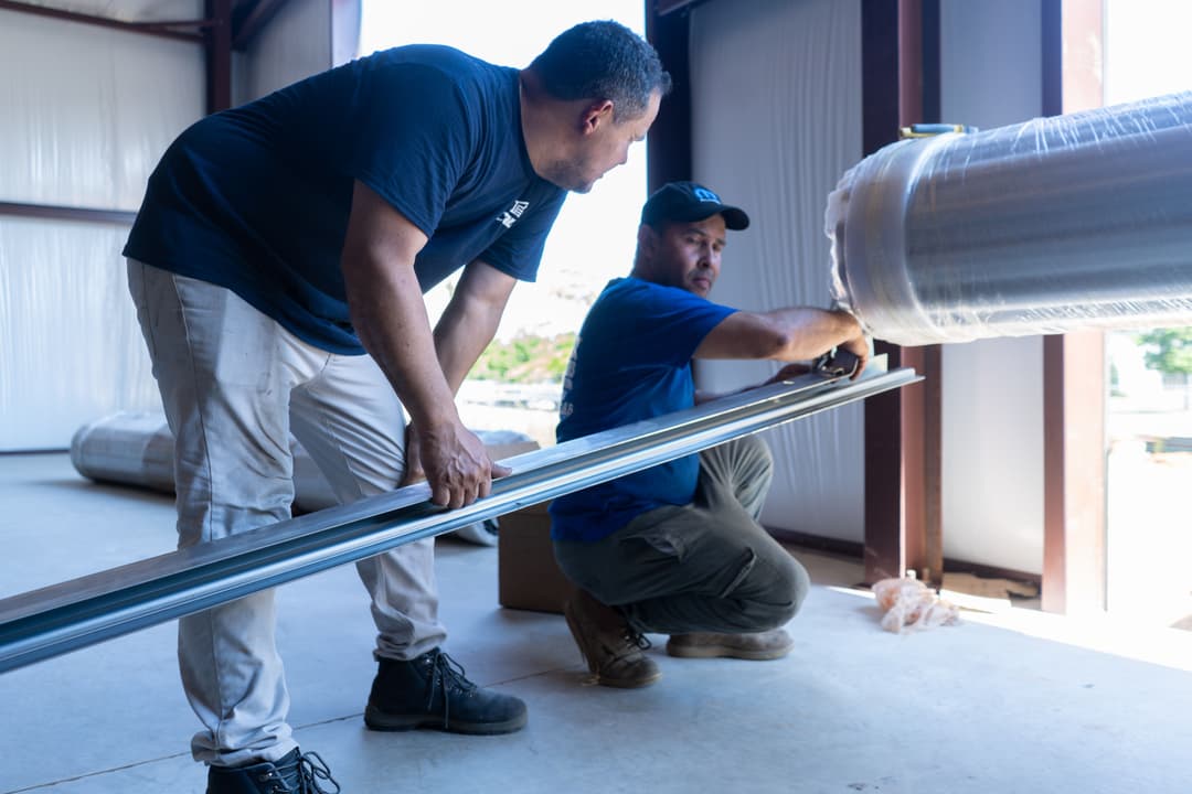 Two workers measuring metal components in a construction site, showcasing teamwork and precision.