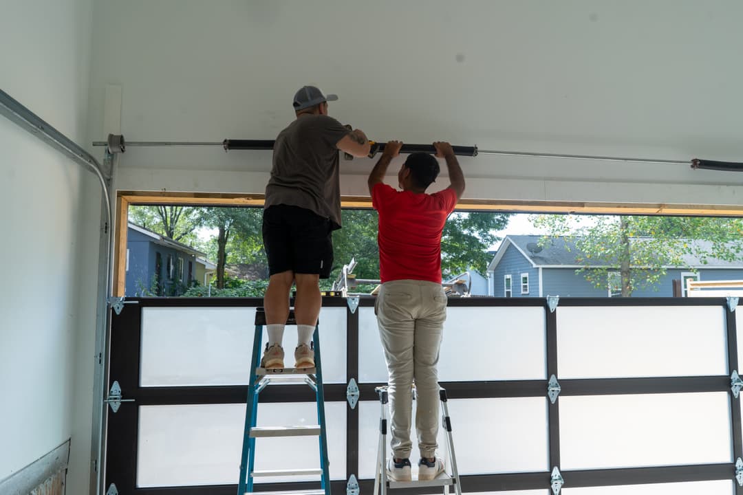 Two men installing a garage door system using ladders in a bright, modern garage.