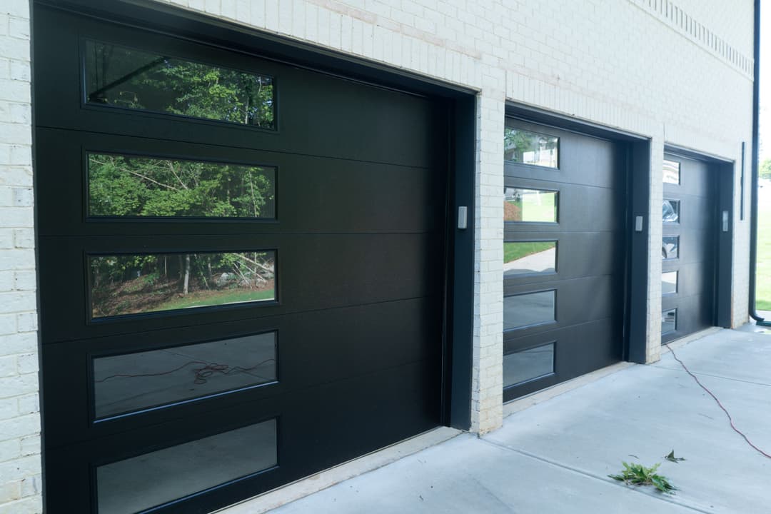 Modern black garage doors with windows on a brick building, enhancing curb appeal.