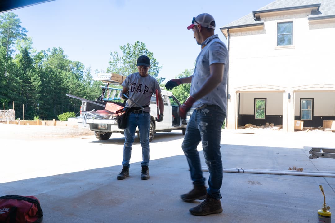 Two construction workers in a garage preparing for a project on a sunny day.