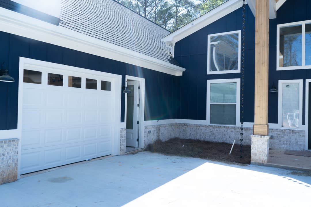 Modern blue house exterior with garage, porch, and landscaped yard. Sunlight casting shadows.