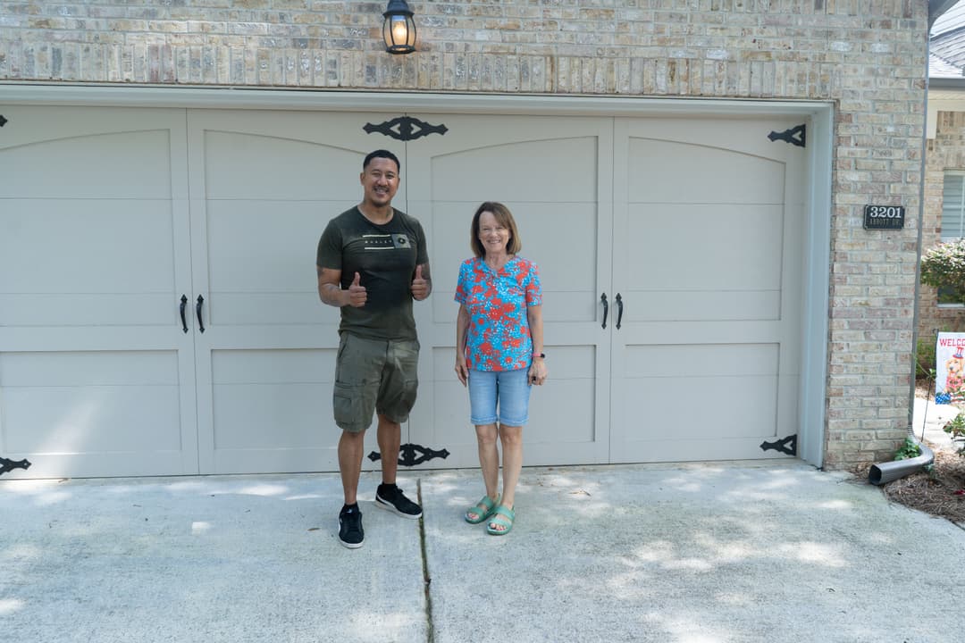 Two people standing in front of a garage door, one giving a thumbs up, smiling.