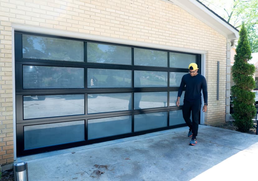 Modern glass garage door with a man in a black outfit and yellow cap walking beside it.